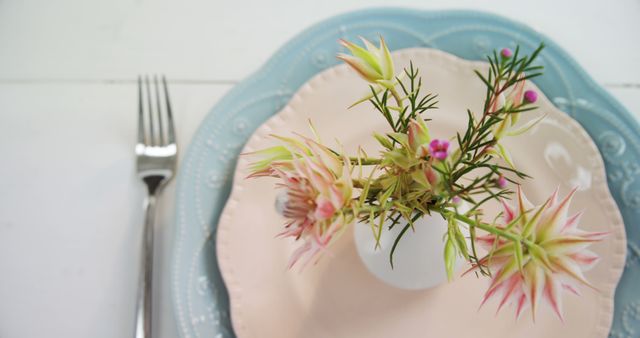 A table setting features a delicate floral arrangement on a pastel plate, with a fork to the side, creating an inviting atmosphere for a meal. The simplicity and elegance of the setup suggest a special occasion or a fine dining experience.
