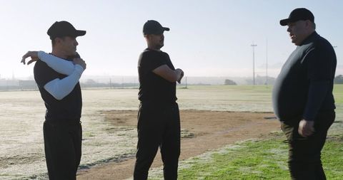 Coach instructing adult baseball players on dewy morning field during team training session