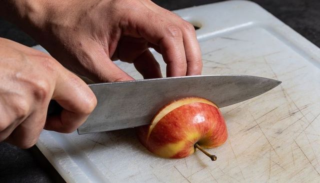 Slicing ripe red-yellow apple with chef knife on plastic cutting board