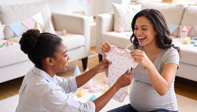 Expectant mother receiving onesie gift at cozy baby shower with friends and pastel decor