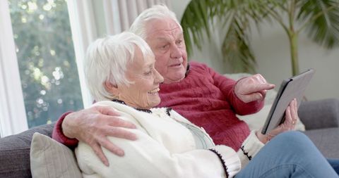 Senior Couple Relaxing on Sofa by Large Window with Tablet - Download Free Stock Images Pikwizard.com