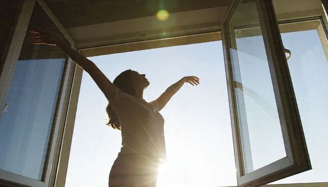 Woman stretching in open casement window with morning sunlight and lens flare silhouette