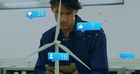 Engineer inspecting wind turbine model with tablet and social media notifications in lab