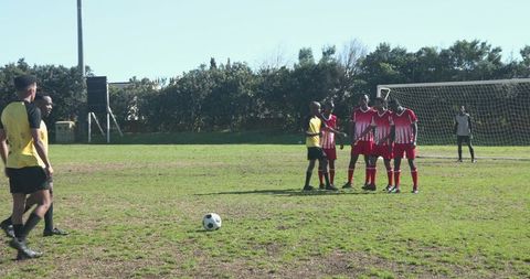 Soccer players forming defensive wall during free kick on sunny day
