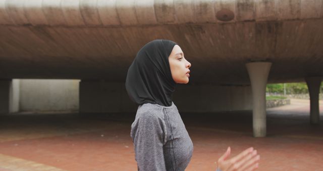 Side view of a biracial woman wearing sportswear and hijab, exercising outdoors in the city on a sunny day, running in slow motion