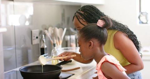 African american mother teaching daughter cooking together pouring batter into pan