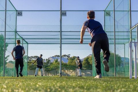 Young cricketers practicing in outdoor net cages with bowler running in and batsman ready