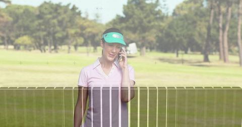 Mature woman talking on smartphone while walking golf fairway wearing green visor and pink polo