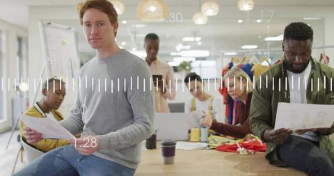 Red-haired designer reviewing fashion sketches in collaborative open-plan studio