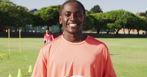 Smiling Athlete Holding Football in Outdoor Practice Field