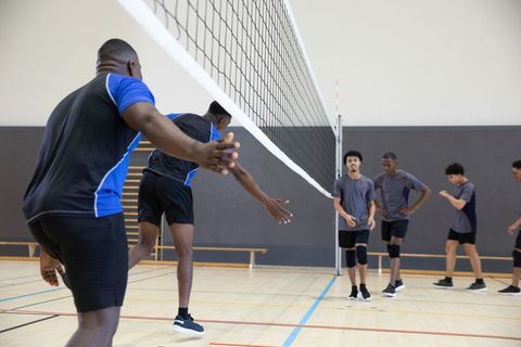 Diverse teen athletes practicing volleyball drill, reaching and blocking at indoor court
