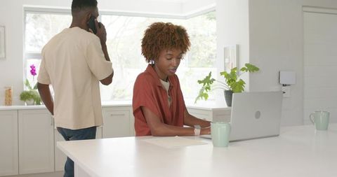 Couple doing remote work at bright kitchen island, woman typing on laptop, man on phone