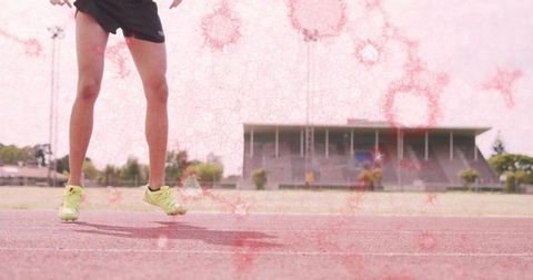 Sprinter neon yellow shoes hitting track lane outside stadium with pink light overlay