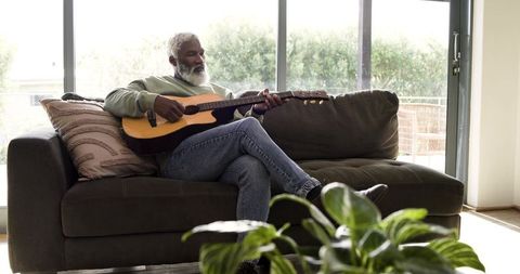Senior Man Relaxing with Guitar by Sunny Glass Door