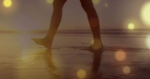 Walking barefoot on wet sand during golden hour with sun bokeh and reflections