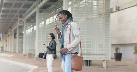 Diverse commuters at transit curb, young man checking smartphone with tan crossbody bag