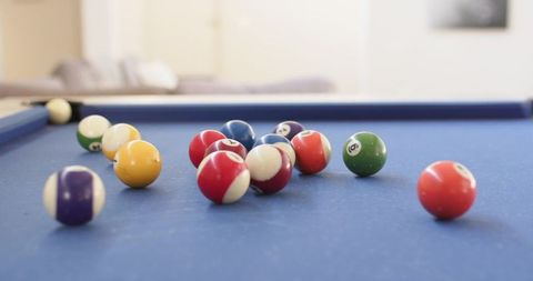 Glossy billiard balls scattering across blue felt pool table in modern lounge interior