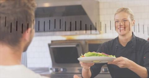 Smiling female chef handing fresh salad across kitchen pass for restaurant hospitality service