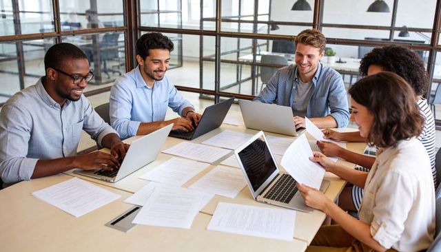 Collaborative team working on laptops and documents in modern glass-walled meeting room