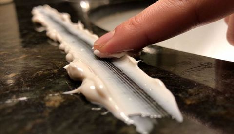 Finger smearing shaving cream from razor cartridge on dark granite countertop closeup