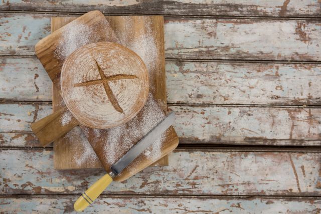 Bread loaf with wheat flour and knife on wooden board