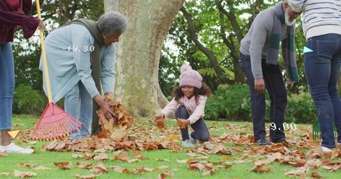 Multigenerational family raking leaves together in autumn park, seasonal outdoor bonding