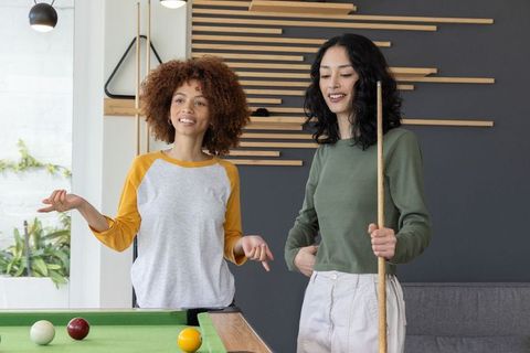 Playing pool together in modern lounge smiling female friends enjoying casual billiards