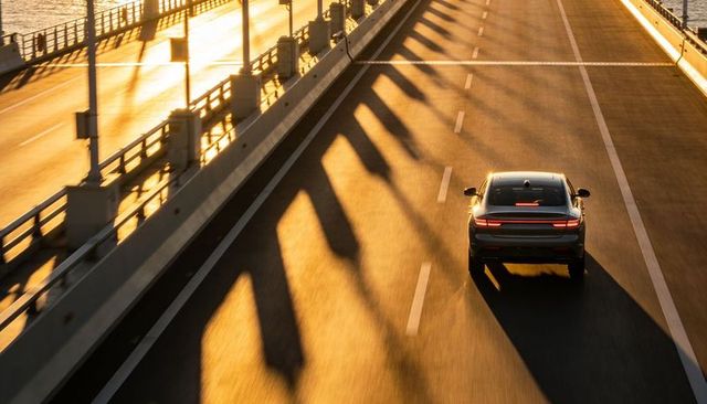 Sunset driving on bridge with long diagonal shadows and modern sedan in golden hour