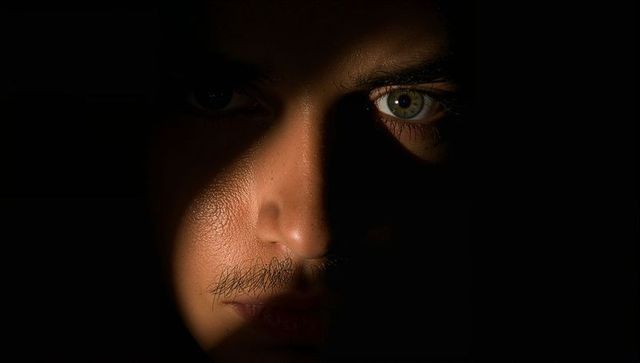Moody chiaroscuro closeup capturing intense green eye and shadowed male face, cinematic