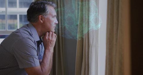 Contemplative mature man gazing out window with ethereal green mist, reflective mood
