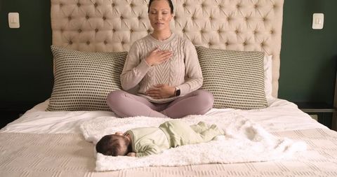 Young mother meditating with relaxed infant at home on comfortable bed