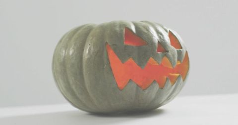 Glowing carved gray-green pumpkin casting warm orange light on white tabletop halloween