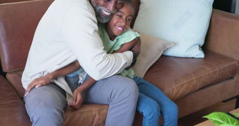 Older man hugging teenage girl on leather sofa sharing warm cozy family moment