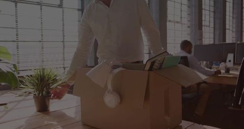 Office worker packing belongings in cardboard box on desk