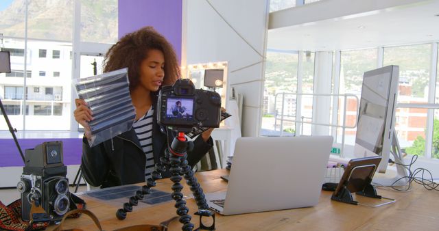 Woman reviews photography accessories in bright, contemporary studio with camera on tripod. Ideal for highlighting modern tech use, blog content, influencer lifestyle, social media campaigns, digital content creation, and professional product review channels.
