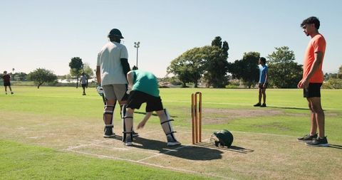 Multicultural cricket players adjusting stumps on park pitch, preparing for next delivery