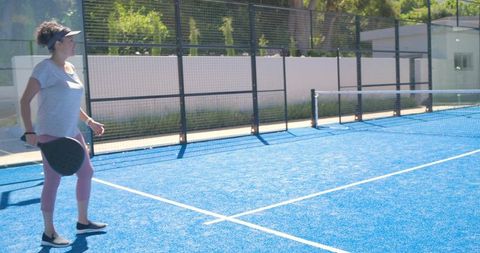 Woman checking phone holding paddle on vibrant blue padel court for active lifestyle
