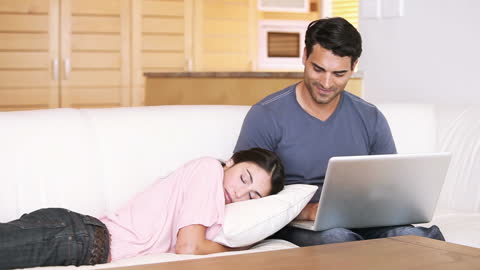 Man Working on Laptop Next to Sleeping Girlfriend on Couch