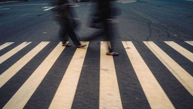 Walking blurred pedestrians crossing zebra crosswalk at urban intersection, motion blur