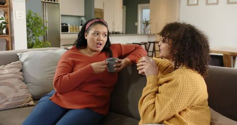 Friends Chatting on Sofa Holding Coffee Mugs in Cozy Open-Plan Living Room
