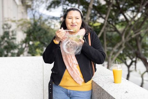 Mature woman enjoying healthy salad lunch outdoors in urban plaza casual style
