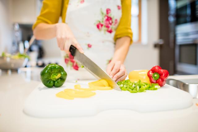 Mid section of woman cutting vegetables on chopping board in kitchen