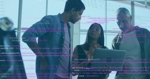 Software team examining code on laptop leaning over workstation in bright glass office
