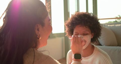 Multiracial friends applying face mask and laughing during cozy at-home spa moment