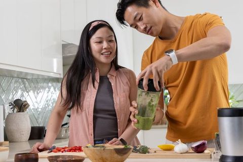 Young couple preparing green smoothie together in bright modern kitchen, smiling