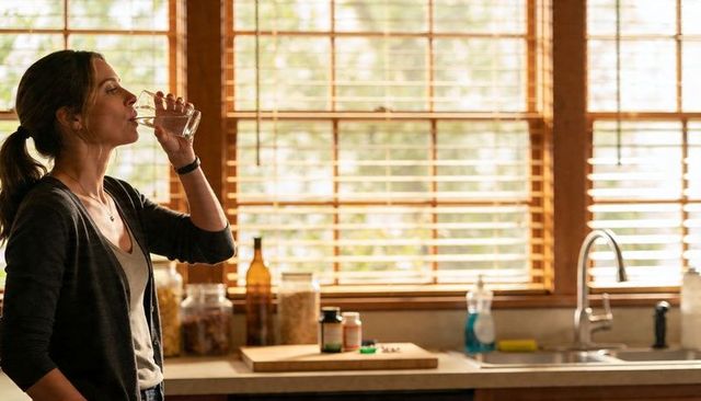 Woman drinking water in sunlit kitchen relaxing morning hydration