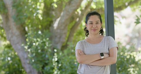 Confident woman leaning on porch post wearing smartwatch enjoying sunny green backyard