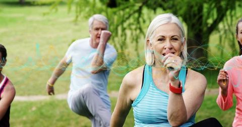 Mid-adult woman leading outdoor group exercise class in park raising knee wearing fitness tracker
