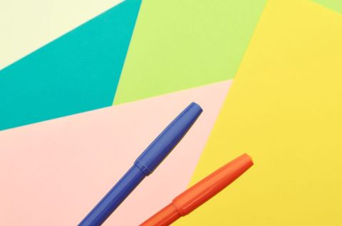 Bright blue and orange pens on colorful geometric paper background for stationery design