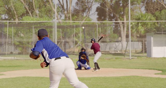 Baseball player pitching ball towards batter on Bsunny day. Picture captures action and intensity of backyard baseball game. Suitable for blog posts about summer sports, baseball-focused websites, children playing sports, and articles on team sports and active hobbies.